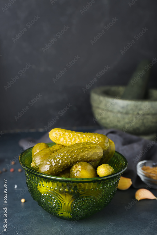 Bowl of tasty canned cucumbers with spices on black table