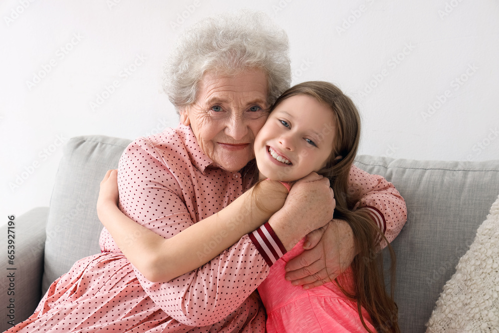 Little girl with her grandmother hugging on sofa at home