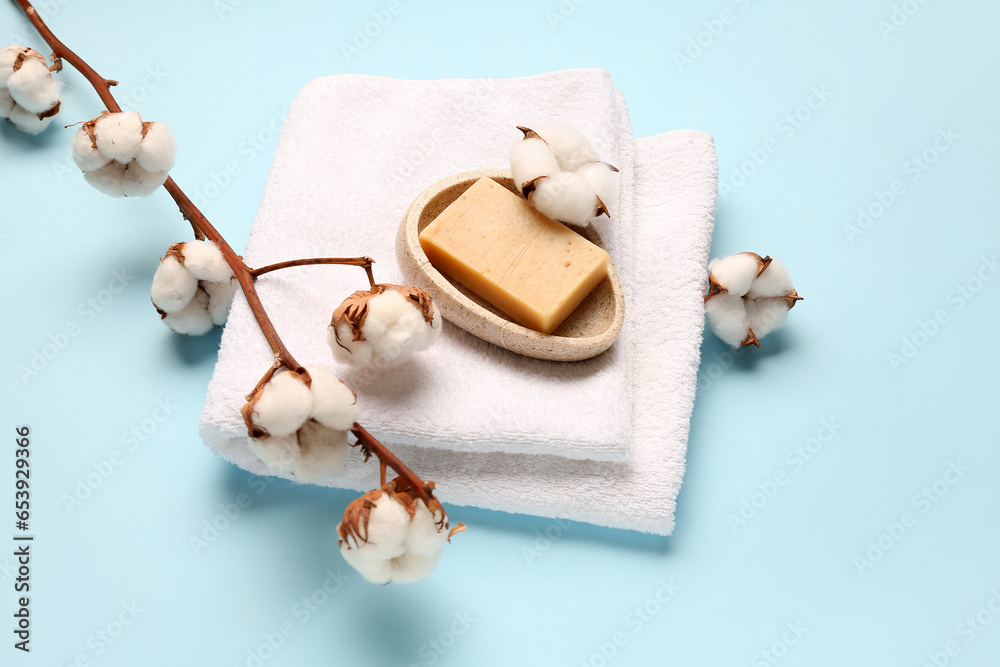 Soap bar, clean towel and cotton branch on color background