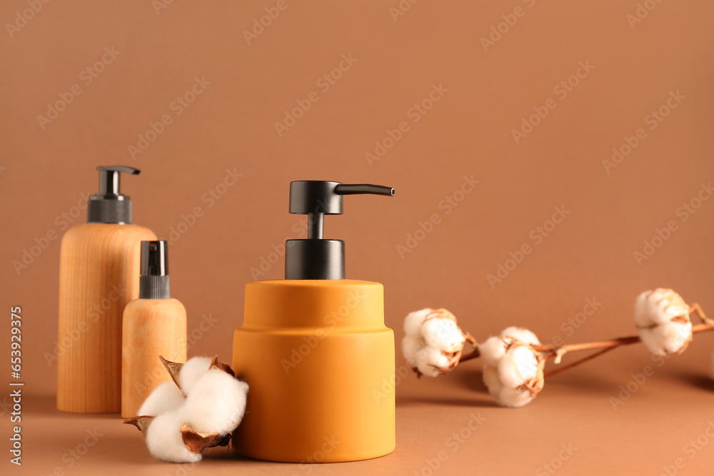 Bottles of cosmetic products with cotton flowers on color background