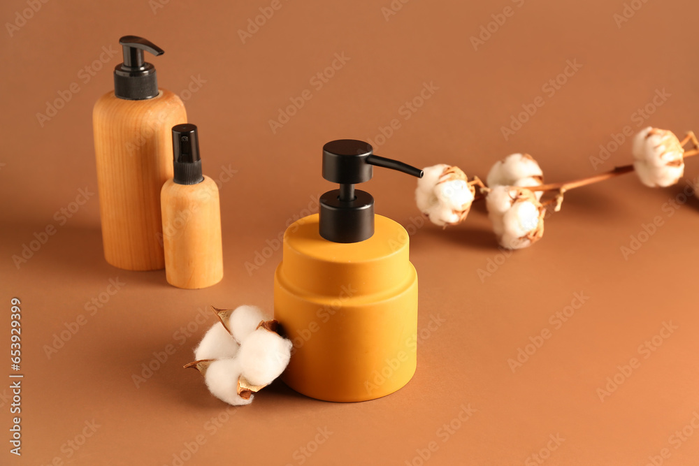 Bottles of cosmetic products with cotton flowers on color background