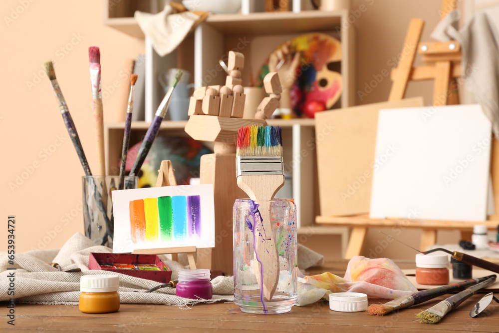 Glass with brushes, paints and mini easel in artists studio