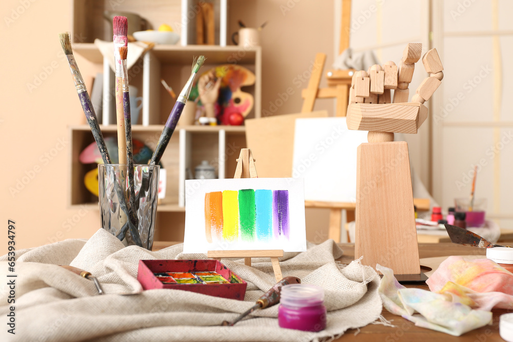 Glass with brushes, paints and mini easel in artists studio