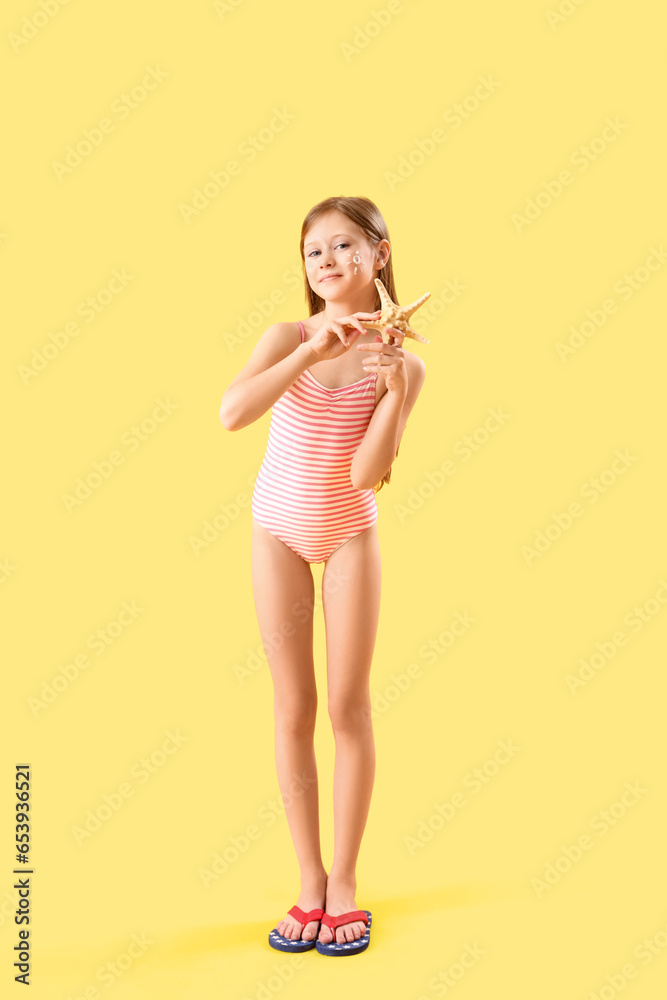 Little girl with starfish and sunscreen cream on her face on yellow background