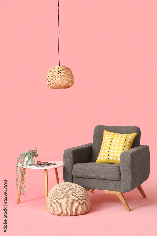 Brown armchair with pouf, table and lamp on pink background