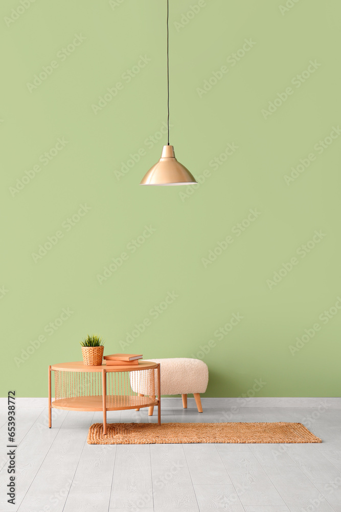 Wooden coffee table with houseplant, books, lamp and pouf near green wall