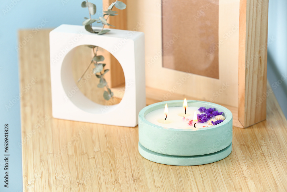 Holder with burning candle and decor on table near blue wall in room, closeup