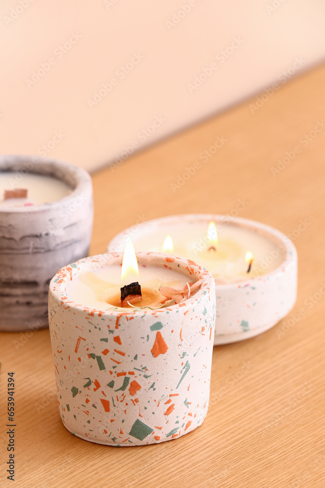 Holders with burning candles on table near beige wall in room, closeup