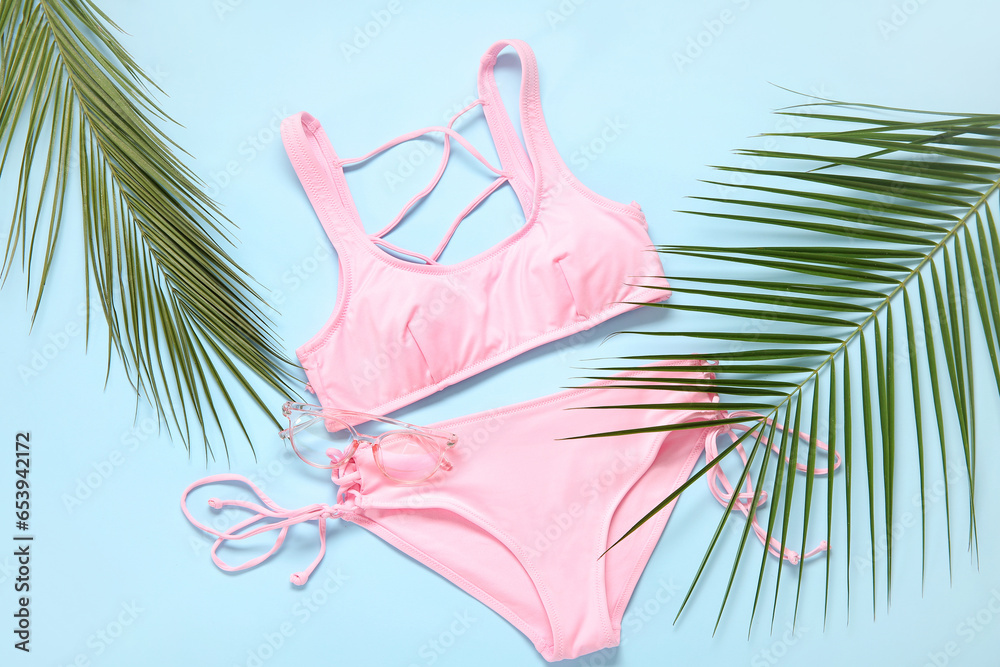 Stylish swimsuit and palm leaves on color background