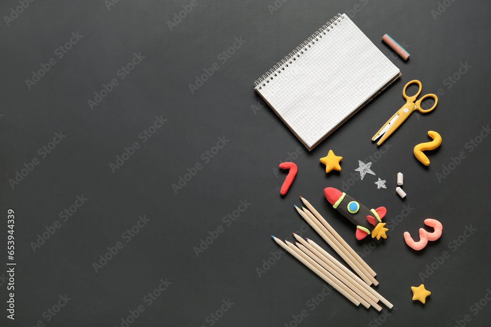 Blank notebook with rocket made of plasticine and different stationery on black chalkboard