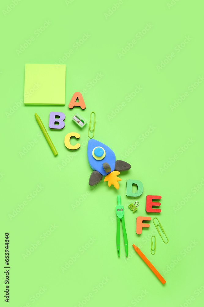 Rocket made of plasticine with wooden letters and stationery on green background