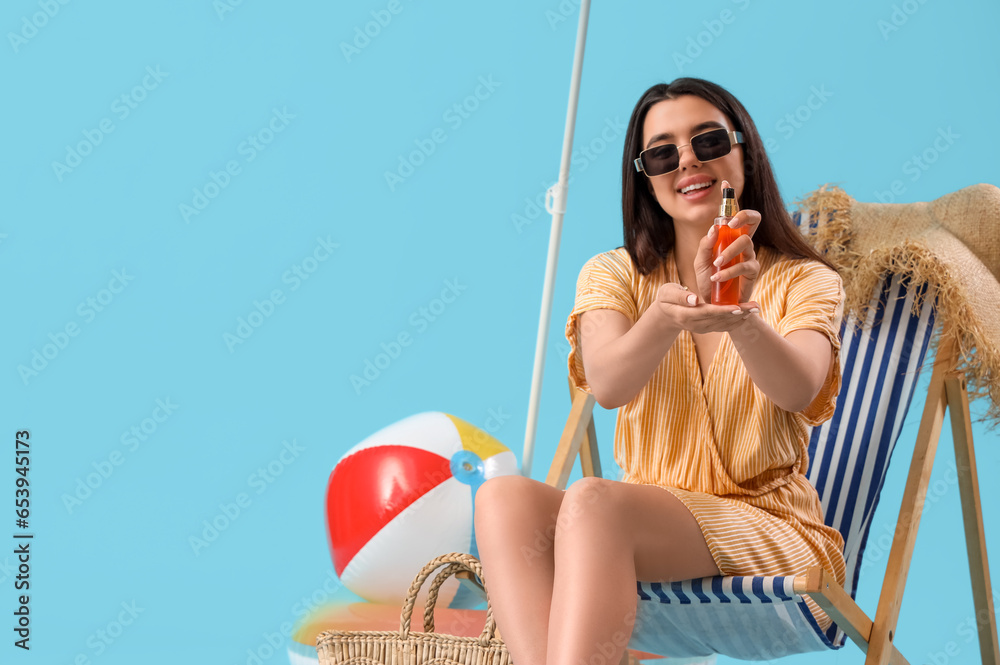 Young woman with sunscreen cream in deck chair on blue background