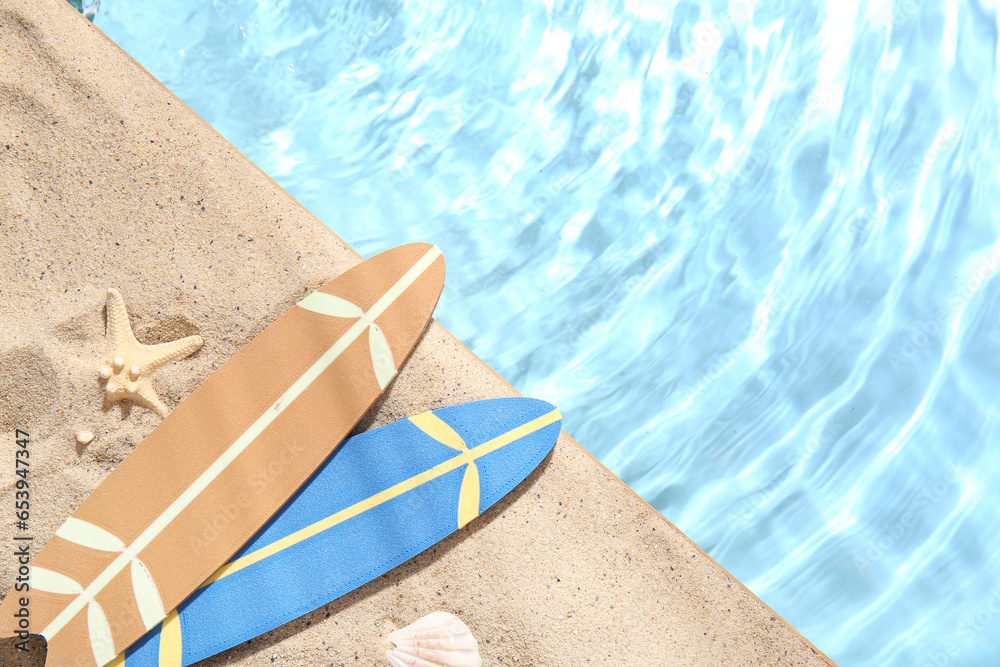 Mini surfboards with starfish and seashell on sand near water