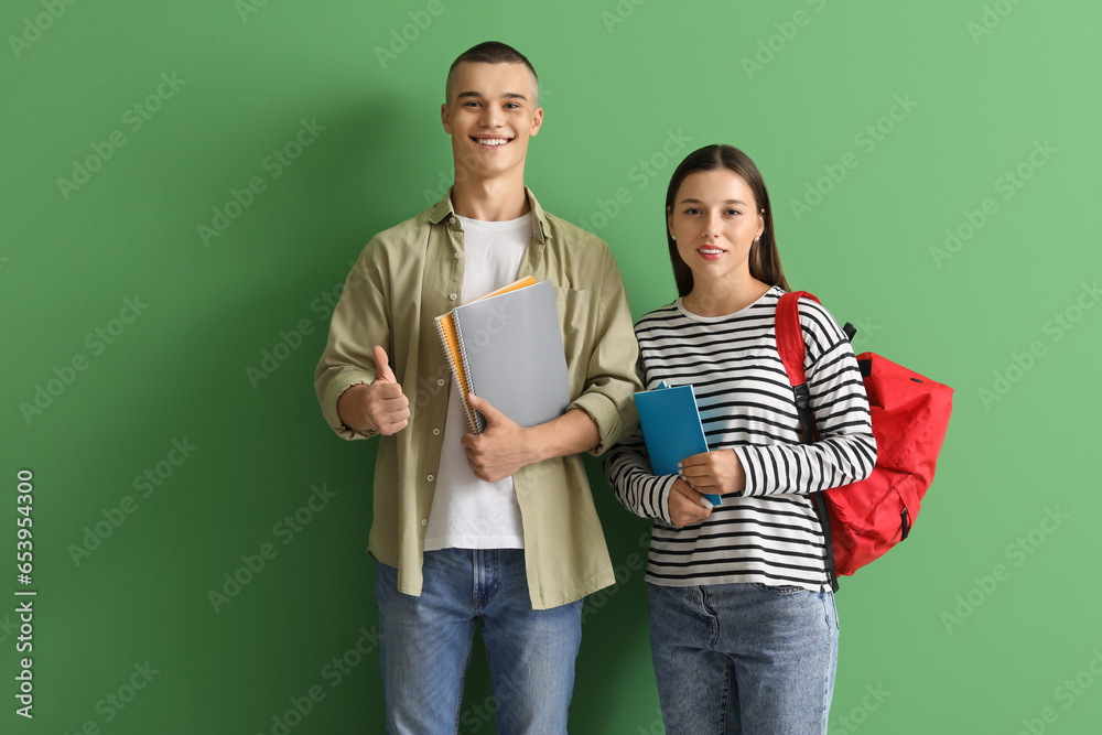 Happy students with backpack and notebooks showing thumb-up gesture on green background