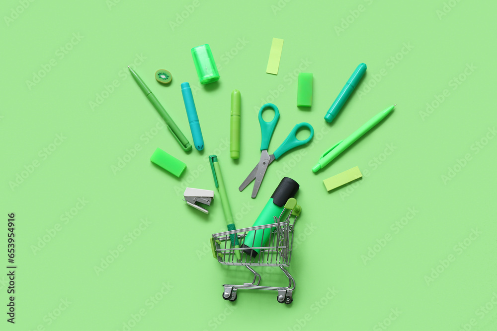 Shopping cart with different stationery on green background