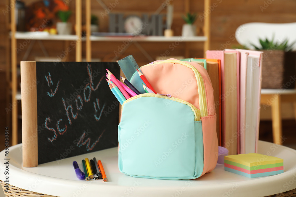 School backpack with stationery and books on table in room