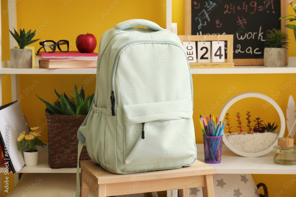 Stylish school backpack near shelf unit with stationery and decor in room