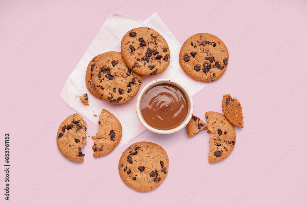 Tasty cookies with chocolate chips and bowl of sauce on pink background