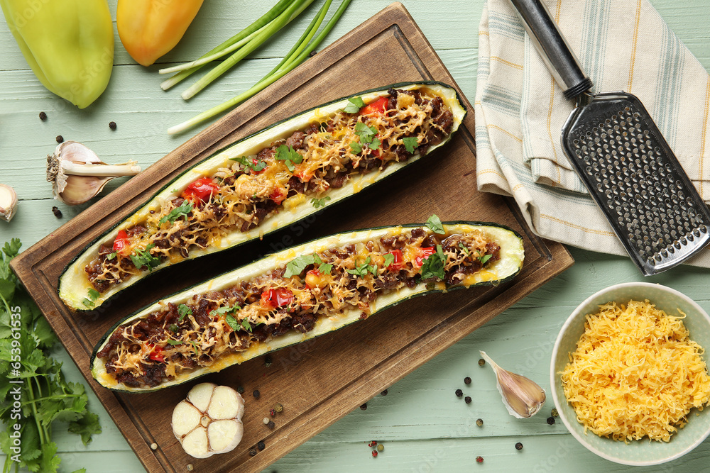 Board with meat stuffed zucchini boats and ingredients on green wooden background