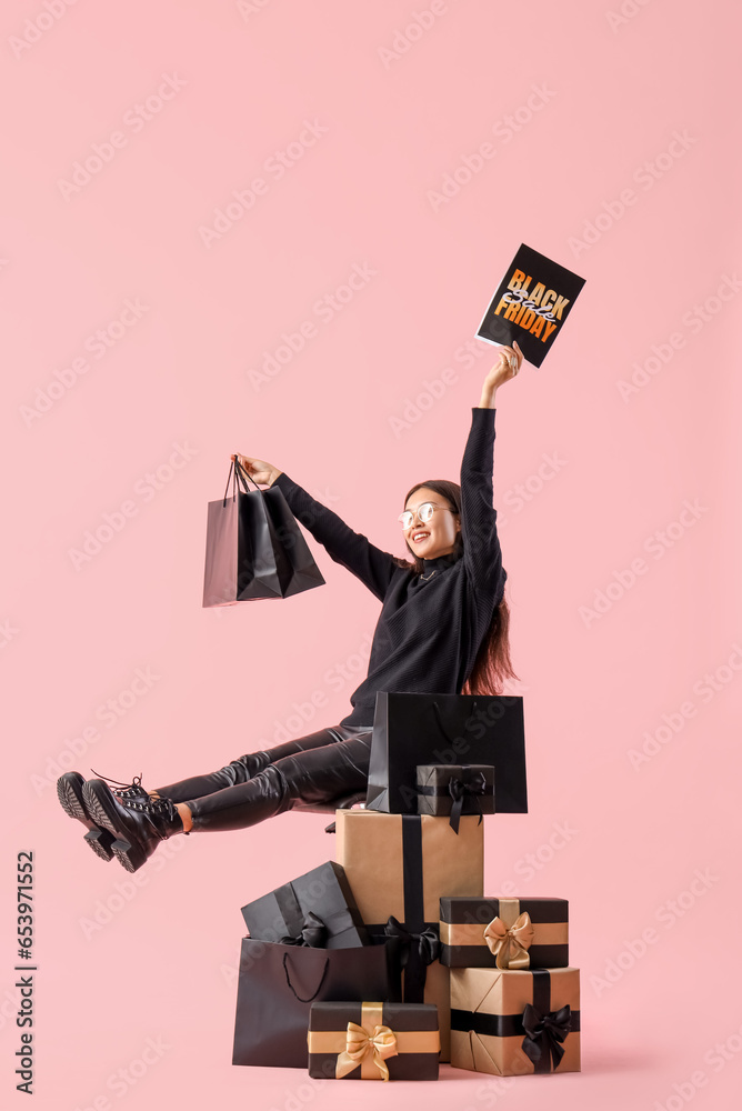 Young Asian woman with shopping bags and gifts on pink background. Black Friday sale