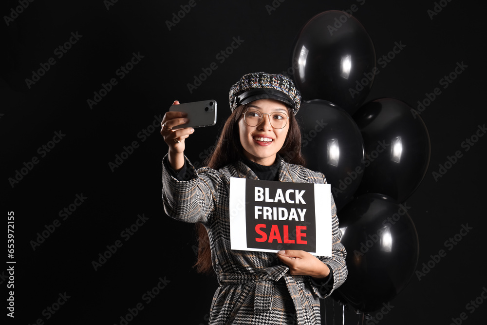 Young Asian woman with card and balloons taking selfie on dark background. Black Friday sale