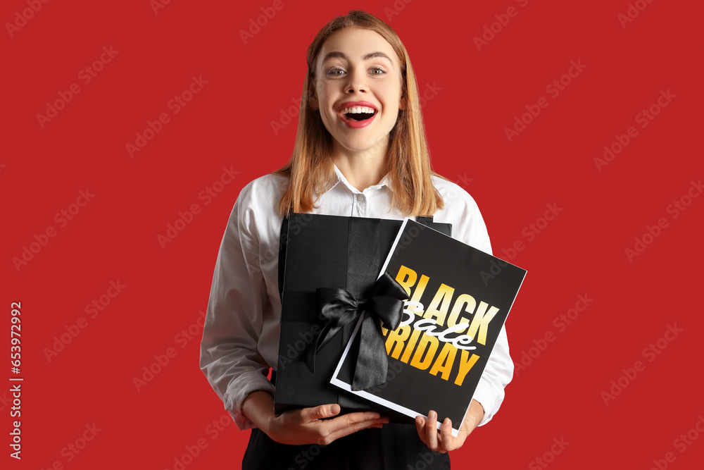 Young woman with card and gift on red background. Black Friday sale