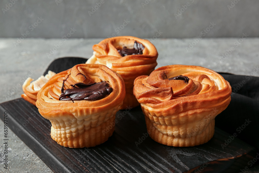 Wooden board of tasty cruffins with chocolate on grey background