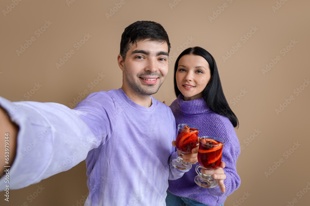 Young couple with glasses of mulled wine taking selfie on color background