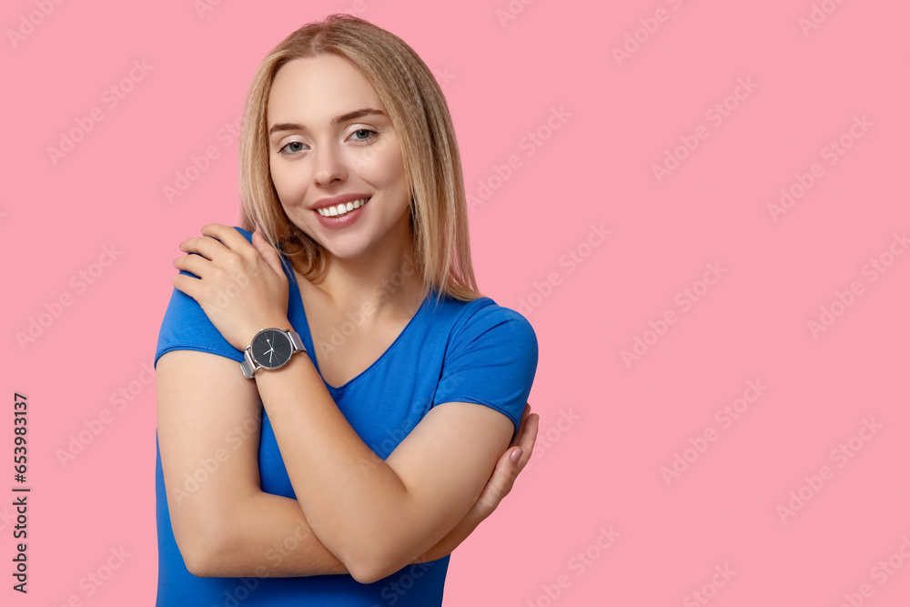 Beautiful young woman embracing herself on pink background