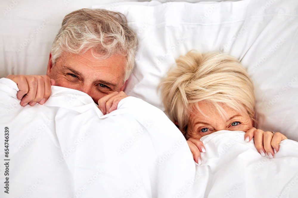 Hiding, portrait and a senior couple in bed for comfort, sleep or love in retirement. Shy, intimate and an elderly man and woman in the bedroom of a house with a blanket covering head in marriage