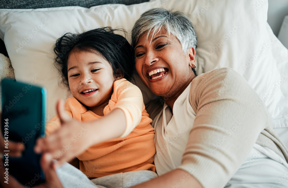 Selfie, smile and old woman with child on bed bonding, relax and love for happy family with care. Photography, technology and grandmother with little girl in bedroom on video call together in home