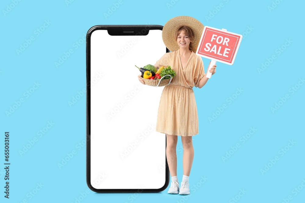 Big smartphone and female farmer with basket full of ripe vegetables and FOR SALE sign on light blue background