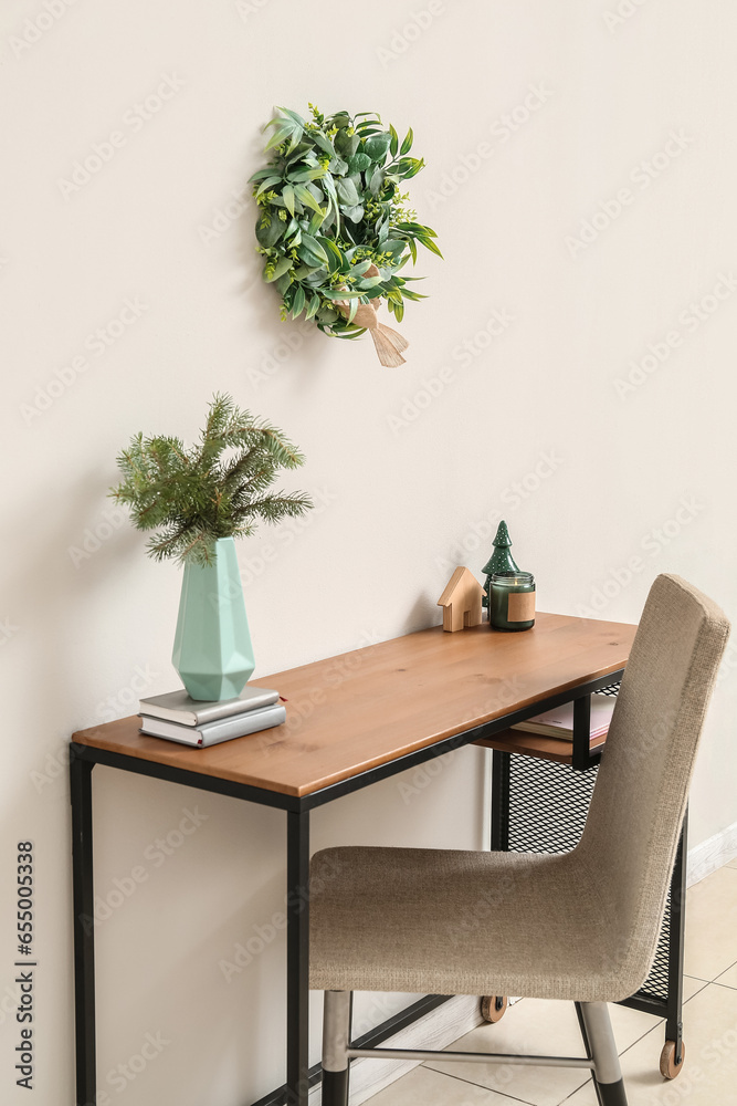 Workplace with fir branches in vase, toys and Christmas mistletoe wreath on light wall