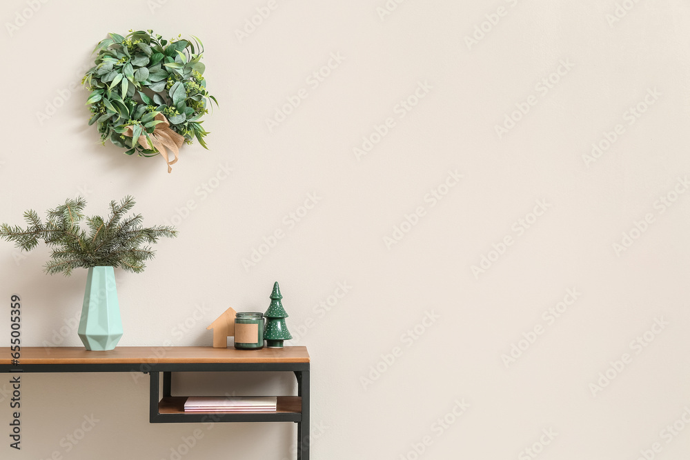 Workplace with fir branches in vase, toys and Christmas mistletoe wreath on light wall