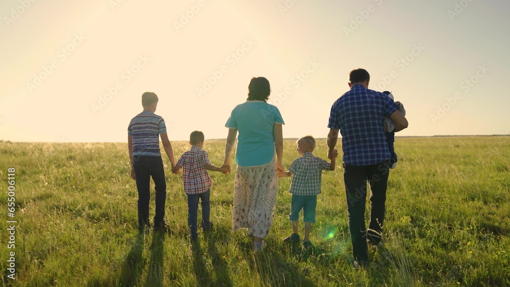 Big family on walk in park. Mom, children, dad are walking along green grass on field. Kid, child, son, boy family team holding hands walk together. Family travel parents children summer in park.