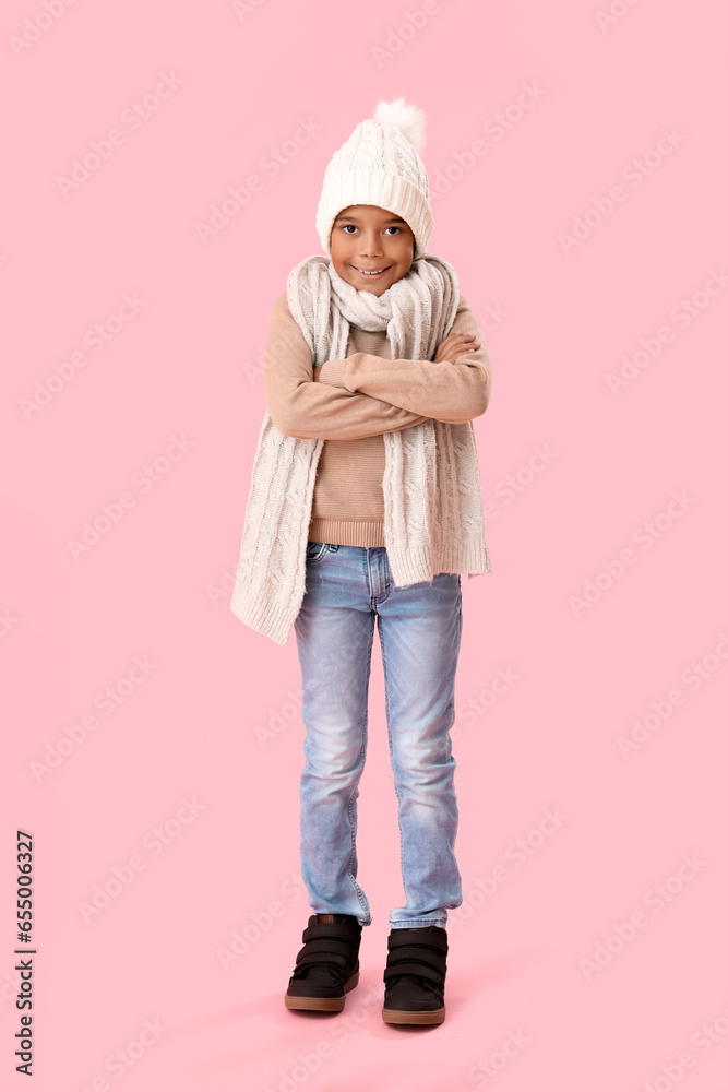 Freezing African-American boy in winter clothes on pink background