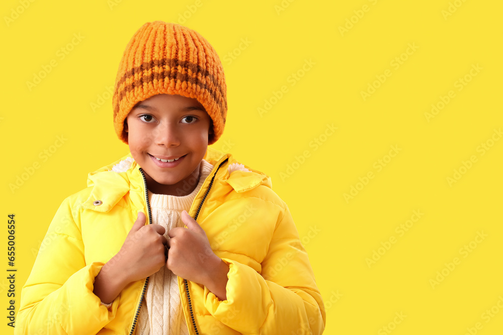 Cute African-American boy in warm winter clothes on yellow background