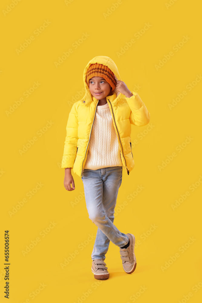 Cute African-American boy in warm winter clothes on yellow background