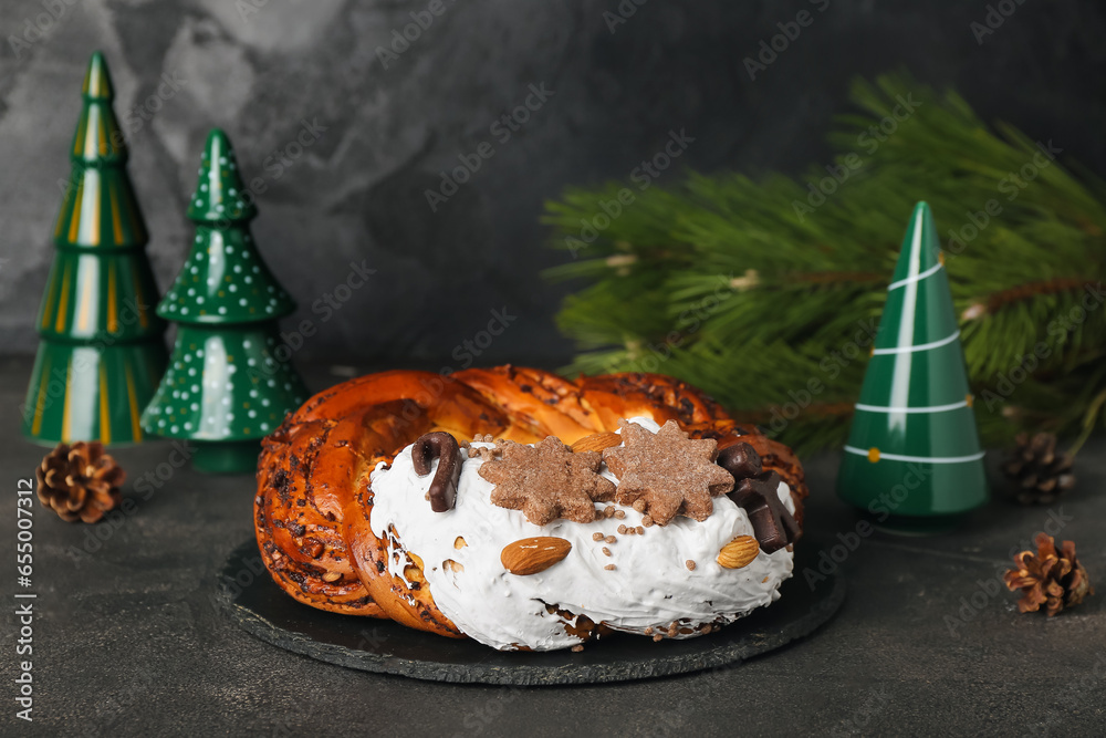 Board with tasty Christmas pastry wreath, coniferous branch and ceramic decorations on dark background