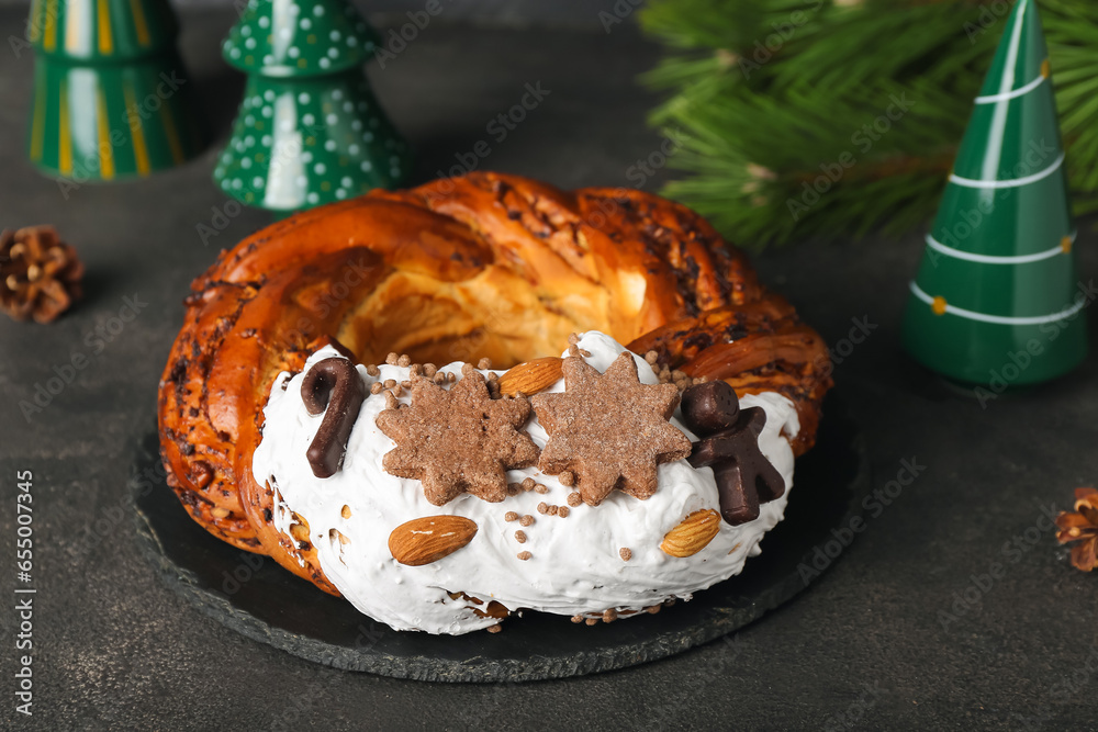 Board with tasty Christmas pastry wreath and ceramic decorations on dark background