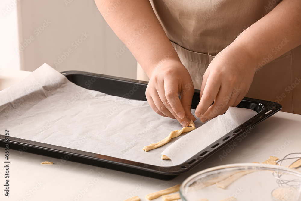 Woman placing Italian Grissini into baking tray at white table in kitchen