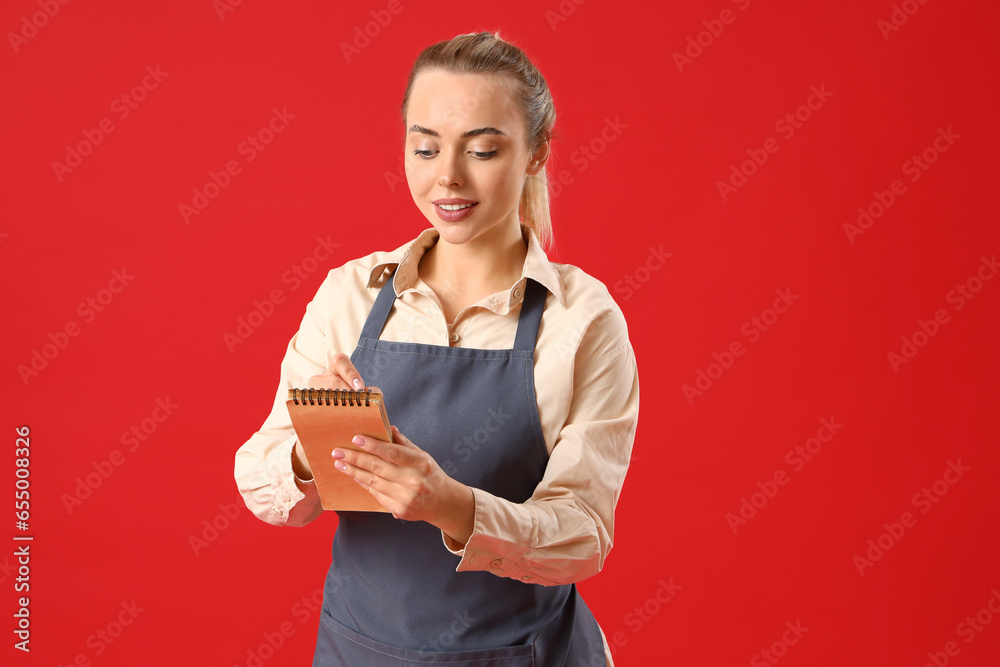 Young barista with notebook on red background