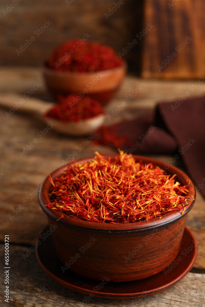 Bowls with pile of saffron on wooden background