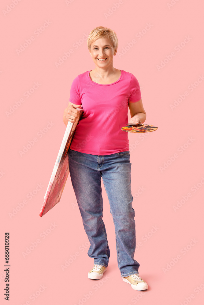 Mature female artist with tools and picture on pink background