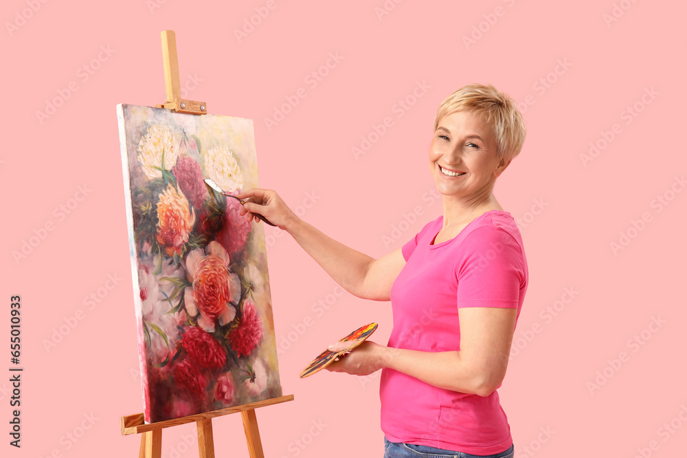 Mature female artist painting picture on pink background