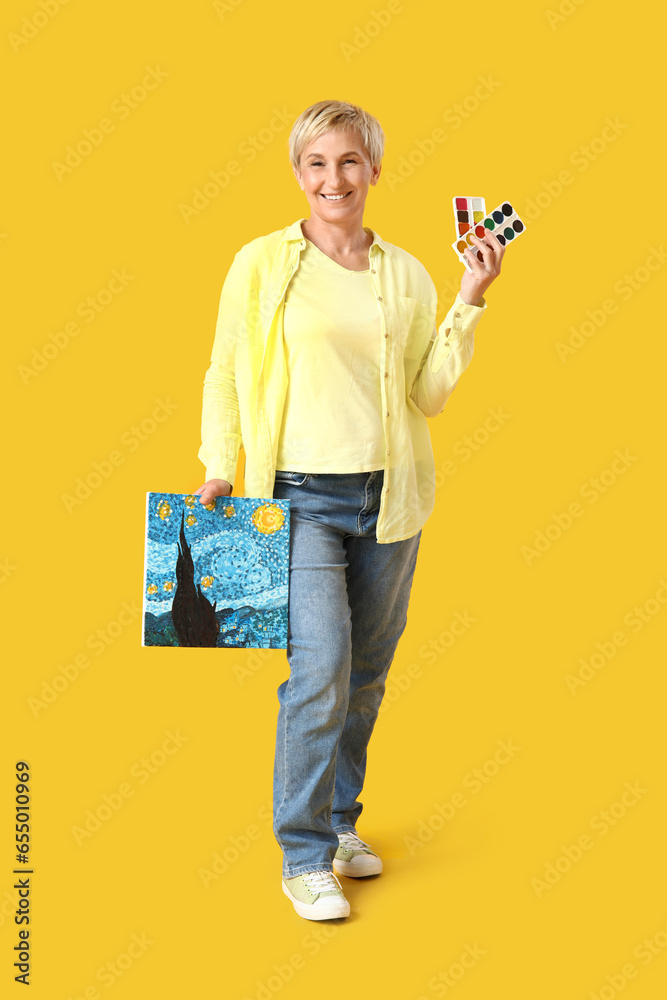 Mature female artist with paints and picture on yellow background