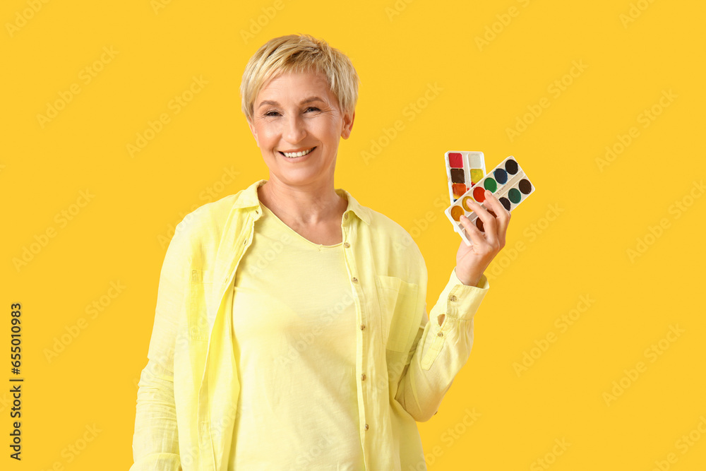 Mature female artist with paints on yellow background