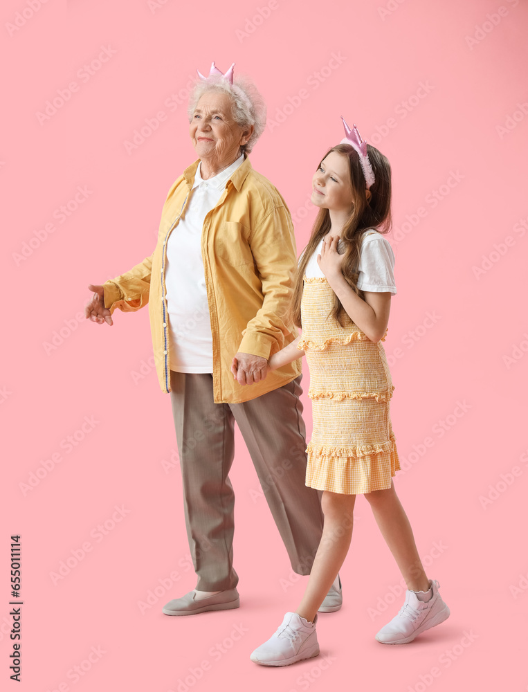 Little girl with her grandmother walking on pink background