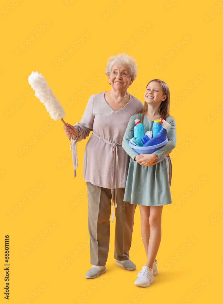 Little girl with her grandmother and cleaning supplies on yellow background