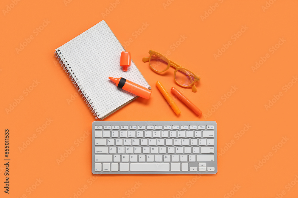 Blank open notebook with eyeglasses, markers and keyboard on orange background